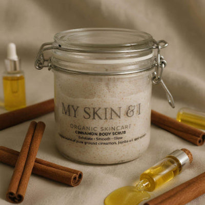 Jar of 'My Skin & I' organic skincare cinnamon body scrub with cinnamon sticks and a dropper on a neutral background
