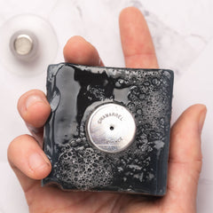 Hand holding a black soap bar with 'Chamarel' branding on a white background
